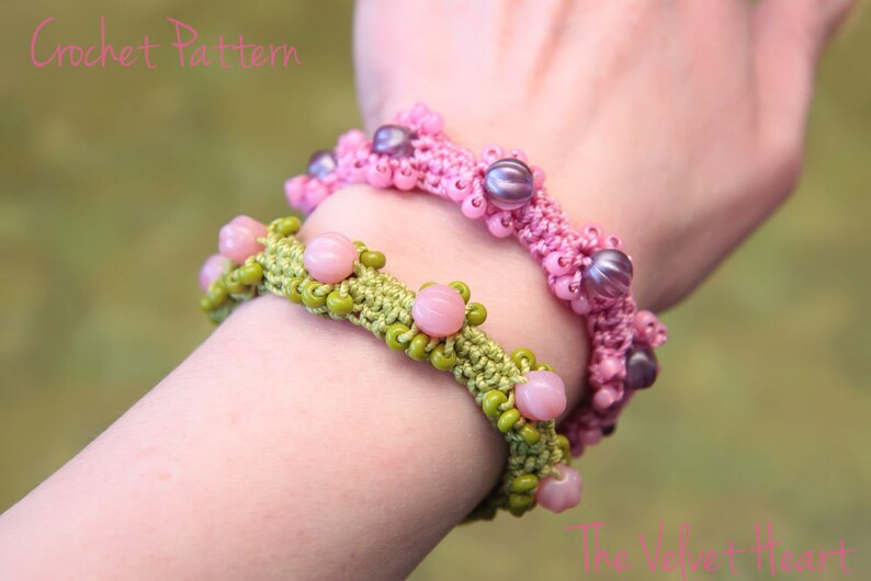 May include: Two crocheted bracelets with beads. The top bracelet is pink with purple beads. The bottom bracelet is green with pink beads. The bracelets are on a person's wrist.