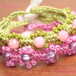 May include: Two crocheted bracelets with pink and green beads. The top bracelet is green with pink beads and the bottom bracelet is pink with purple beads.