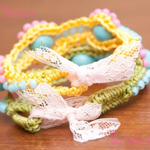 May include: A multi-layered crocheted bracelet with yellow, green, and pink yarn. The bracelet is decorated with blue and pink beads and white lace bows.