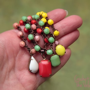 May include: A multi-strand crocheted necklace with colourful glass beads in shades of green, yellow, red, and pink. The necklace features a teardrop-shaped pendant and a square pendant.