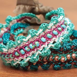May include: Three crocheted bracelets with beads. The top bracelet is white, pink, and turquoise. The middle bracelet is brown and turquoise. The bottom bracelet is turquoise and brown.