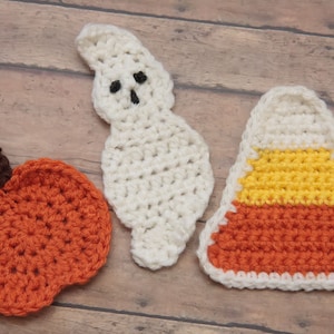 May include: Three crocheted Halloween decorations: a white ghost, an orange pumpkin, and a candy corn with orange, yellow, and white stripes.