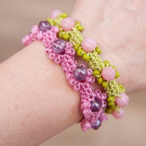 May include: Three crocheted bracelets with pink, green, and purple beads. The bracelets are layered on a person's wrist.