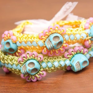 May include: Three colorful crocheted bracelets with turquoise skull beads. The bracelets are layered on top of each other, with the yellow bracelet on top, followed by the green bracelet, and then the pink bracelet.
