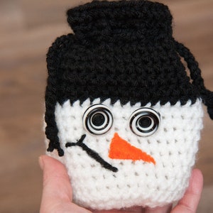 May include: White crocheted snowman ornament with black crocheted hat and a black and white button eyes. The snowman has an orange felt nose.