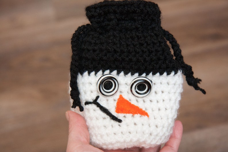 May include: White crocheted snowman ornament with black crocheted hat and a black and white button eyes. The snowman has an orange felt nose.