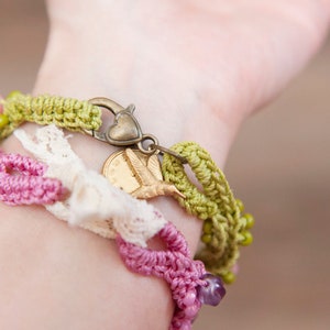 May include: A close-up of a wrist wearing a layered bracelet set. The bracelet set features a green crocheted bracelet with a heart-shaped clasp, a white crocheted lace bracelet, and a pink crocheted bracelet with purple beads. A gold hummingbird charm hangs from the green bracelet.