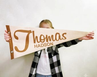 May include: A triangular felt pennant flag in cream with a brown border and two metal grommets on the left side. The text "Thomas" is printed in a large brown script font, with the name "HADSON" printed below in a smaller brown block font.