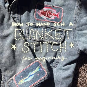 May include: A denim jacket with two fish patches and the text "HOW TO HAND SEW A BLANKET STITCH for beginners". The patches feature colourful fish designs with red, pink, and blue accents. The jacket has a pocket and star details.