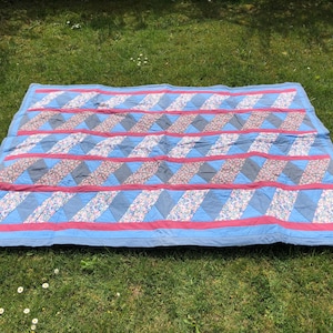 Könnte beinhalten: Eine Patchwork-Decke mit einem blauen, rosa und weißen Blumenmuster. Die Decke besteht aus Quadraten und Rechtecken, die diagonal zusammengenäht sind.