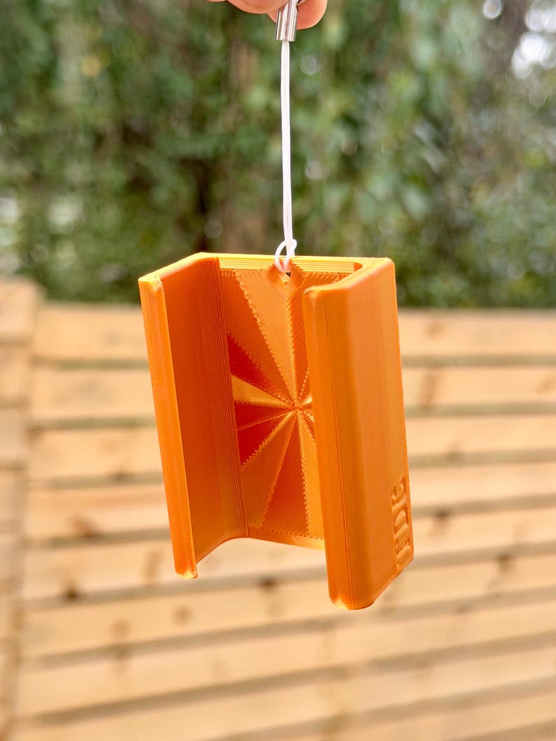 Pu&ograve; includere: Un oggetto arancione, stampato in 3D, a forma di libro pieghevole, con un cordino bianco attaccato. L'oggetto ha un design geometrico all'interno e la parola "IDE" &egrave; stampata sul lato. L'oggetto &egrave; sospeso in aria.