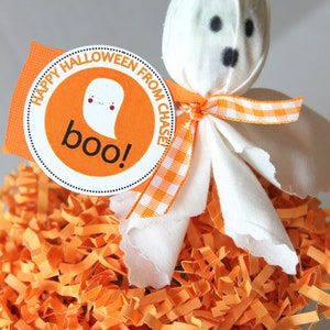 Pode incluir: Um fantasma de tecido branco com olhos pretos e uma fita xadrez vermelha e branca. O fantasma est&aacute; sentado em um balde cheio de papel picado laranja. Uma etiqueta redonda laranja com o texto "Feliz Halloween do Chase! Boo!" est&aacute; presa ao fantasma.