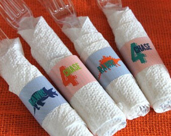 May include: Four white napkins with colorful printed designs wrapped around plastic forks. The designs include a dinosaur, a paw print, and the name "Chase".