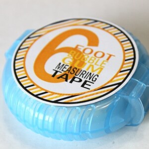 May include: A blue plastic measuring tape with a white label that says "6 Foot Bubble Gum Measuring Tape". The label has black and yellow stripes.