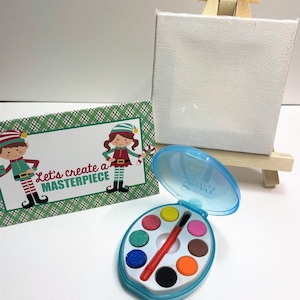 May include: A small easel with a blank canvas, a set of watercolors in a blue case with a brush, and a card with the text "Let's create a masterpiece" featuring two elves.