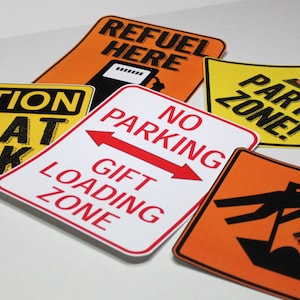 May include: A set of eight construction-themed party signs with yellow, orange, and white backgrounds. The signs feature black text and graphics, including "Refuel Here", "Party Zone", "Caution Kids At Work", "No Parking", "Gift Loading Zone", and "Dig In!"