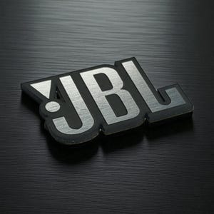 Könnte beinhalten: Schwarzes und silbernes JBL-Logo. Die Buchstaben JBL sind in gebürsteter Silberoptik auf schwarzem Hintergrund gehalten. Das Emblem ist leicht angewinkelt, mit einem dezenten Schatteneffekt.