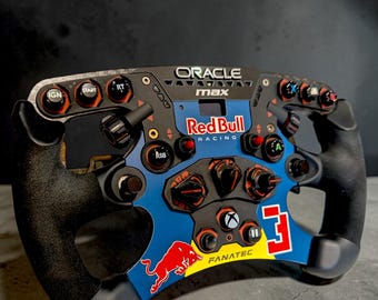 Könnte beinhalten: Ein schwarz-blaues Rennlenkrad mit dem Red Bull Racing Logo und der Nummer 3. Das Lenkrad hat mehrere Knöpfe und Drehregler, mit dem Text "ORACLE max" oben. Entworfen für ein Fanatec-System.