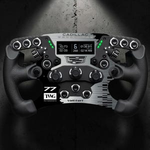 May include: A black and silver Cadillac racing steering wheel featuring a digital display showing race data, multiple control buttons, rotary dials, and the text Cadillac, 77 TWG Motorsports, and Valtteri printed on the front face.