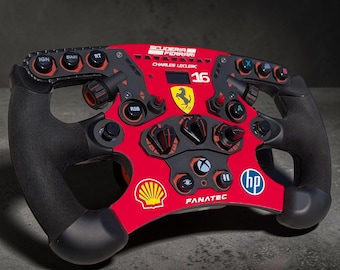 May include: A red and black racing steering wheel controller featuring the Scuderia Ferrari logo, the number 16, and the name Charles Leclerc. The device includes various buttons, rotary dials, and logos for Shell, HP, and Fanatec, with textured black grips.