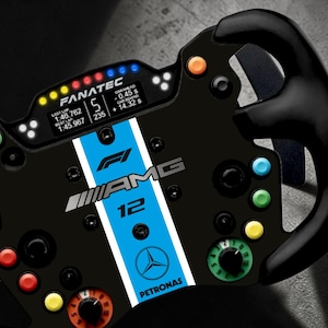 Può includere: Un volante da corsa Fanatec nero con una striscia centrale azzurra che riporta i loghi F1, AMG e Mercedes-Petronas, oltre al numero 12. Il volante include un display digitale, diversi pulsanti colorati e manopole rotanti.
