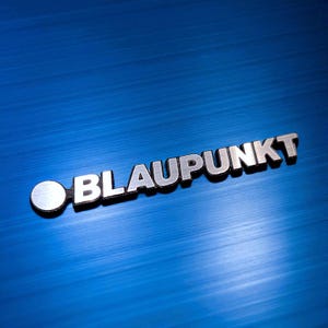Può includere: Logo Blaupunkt argentato con un elemento circolare a sinistra. Il logo è posto su uno sfondo blu vibrante e strutturato. La parola "BLAUPUNKT" è ben visibile.