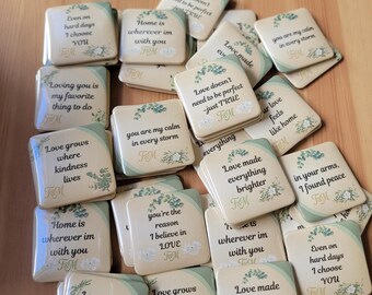 May include: A collection of square ceramic coasters with inspirational quotes in black text, floral accents, and a light beige background. The coasters have a green border and are scattered on a wooden surface.