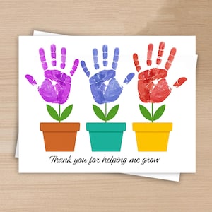 Può includere: Biglietto di auguri con tre fiori fatti con impronte di mani colorate. Le impronte sono viola, blu e rosse, con steli e foglie verdi. I vasi sono marroni, turchesi e gialli. Il testo "Thank you for helping me grow" è in basso.