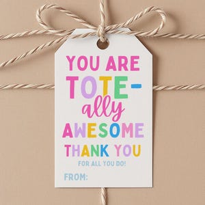 Könnte beinhalten: Ein Geschenk, verpackt in beigem Papier, mit Bindfaden gebunden und einem weißen Anhänger. Der Anhänger lautet "YOU ARE TOTALLY AWESOME THANK YOU FOR ALL YOU DO!" in bunten Buchstaben. Der Anhänger enthält ein Feld für "VON:"
