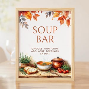 May include: A framed sign with a light wood border featuring the text SOUP BAR, CHOOSE YOUR SOUP, ADD YOUR TOPPINGS, ENJOY! The illustration shows a bowl of soup, a pot, bread, herbs, and tomatoes, decorated with orange and brown autumn leaves.