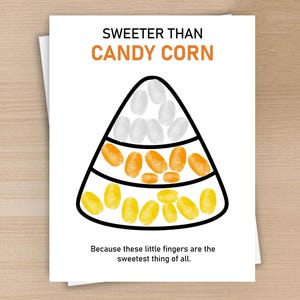 May include: A white greeting card featuring the text SWEETER THAN CANDY CORN at the top and Because these little fingers are the sweetest thing of all at the bottom. A large candy corn outline is filled with white, orange, and yellow fingerprints.