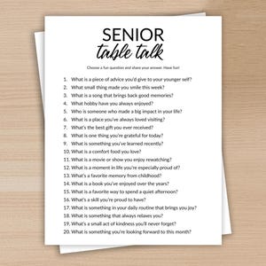 May include: A white paper with the text "SENIOR table talk" and a list of 20 questions. The paper is on a light wood surface. The questions are designed to spark conversation and reflection.