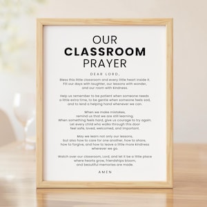 以下が含まれることがあります： 太い黒文字でOUR CLASSROOM PRAYERと書かれ、その下にサンセリフ体のフォントで複数行の祈りの言葉が記された額入りウォールアートプリント。明るい色の木製フレームが、黒い文字が印刷された白い背景を囲んでいます。