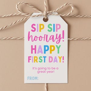 May include: A white rectangular gift tag tied with tan twine, featuring the colorful text "SIP SIP hooray! HAPPY FIRST DAY!" in pink, yellow, green, and blue. Below, it reads "It's going to be a great year!" and "FROM:" in light blue.