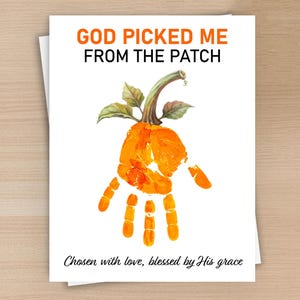 Peut inclure: Une carte de vœux blanche avec le texte orange GOD PICKED ME FROM THE PATCH en haut. En dessous se trouve une empreinte de main orange en forme de citrouille avec une tige et des feuilles vertes. Le texte en bas indique Chosen with love, blessed by His grace.