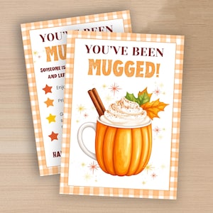 May include: Two autumn-themed cards with orange gingham borders. One card reads "YOU'VE BEEN MUGGED!" with a pumpkin-shaped mug filled with whipped cream and a cinnamon stick. The other card has text and star icons.