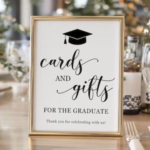 May include: A framed sign with gold trim, featuring the words "cards and gifts" in elegant script, topped with a graduation cap icon. The text "For the Graduate" and "Thank you for celebrating with us!" are also displayed.