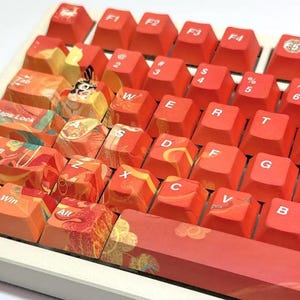 Może przedstawiać: Czerwono-pomarańczowa klawiatura z niestandardowymi klawiszami w japońskim stylu. Klawisze mają fakturowaną powierzchnię i są ozdobione skomplikowanymi wzorami. Klawiatura ma białą ramkę i spację z czerwono-pomarańczowym wzorem.