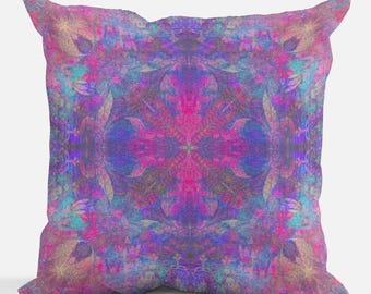 Op de afbeelding: Een decoratief kussen met een kleurrijk, abstract ontwerp in tinten roze, paars, blauw en turquoise. Het patroon is symmetrisch en lijkt op een mandala.
