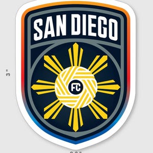 May include: A shield-shaped sticker with the text "SAN DIEGO" in white. The sticker is 3 inches tall and 2.3 inches wide. It features a yellow and white sunburst design with "FC" in the center, set against a navy blue background.