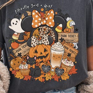 May include: Dark gray t-shirt featuring a Halloween-themed graphic. The design includes a Minnie Mouse-inspired character with a pumpkin, ghost, and other festive elements. Text reads "Literally Just a Girl."