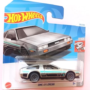Può includere: Auto giocattolo DMC DeLorean argentata Hot Wheels su una carta blu e bianca. L'auto ha dettagli turchese e neri. La carta dice "Hot Wheels" e "DMC DeLorean". L'auto è contrassegnata 3/5 e 236/250.