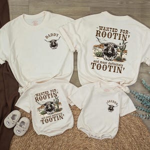 May include: Cream-colored family matching t-shirts and onesies. The adult shirts say "DADDY" and "WANTED FOR ROOTIN' and most definitely TOOTIN'". The baby onesies say "WANTED FOR ROOTIN' and most definitely TOOTIN'" and "JAYDEN".