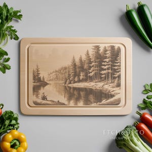 May include: A rectangular wooden cutting board with a sepia-toned engraved image of a person fishing on a lake surrounded by trees. The board has a light wood finish and a recessed juice groove. The text "ETCH&DECO" is at the bottom.