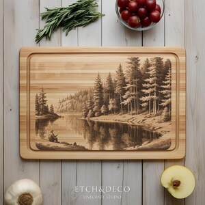 May include: A rectangular wooden cutting board with a recessed edge. The board features a detailed engraved scene of a person fishing on a lake surrounded by pine trees. The text "ETCH & DECO" and "LINECRAFT STUDIO" are at the bottom.