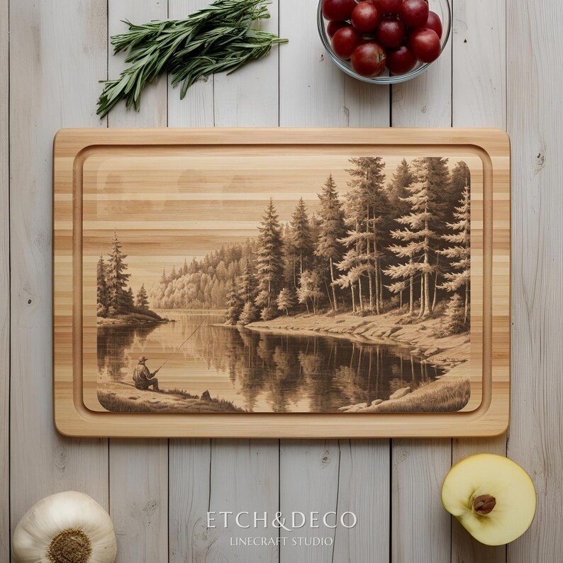 May include: A rectangular wooden cutting board with a recessed edge. The board features a detailed engraved scene of a person fishing on a lake surrounded by pine trees. The text "ETCH & DECO" and "LINECRAFT STUDIO" are at the bottom.