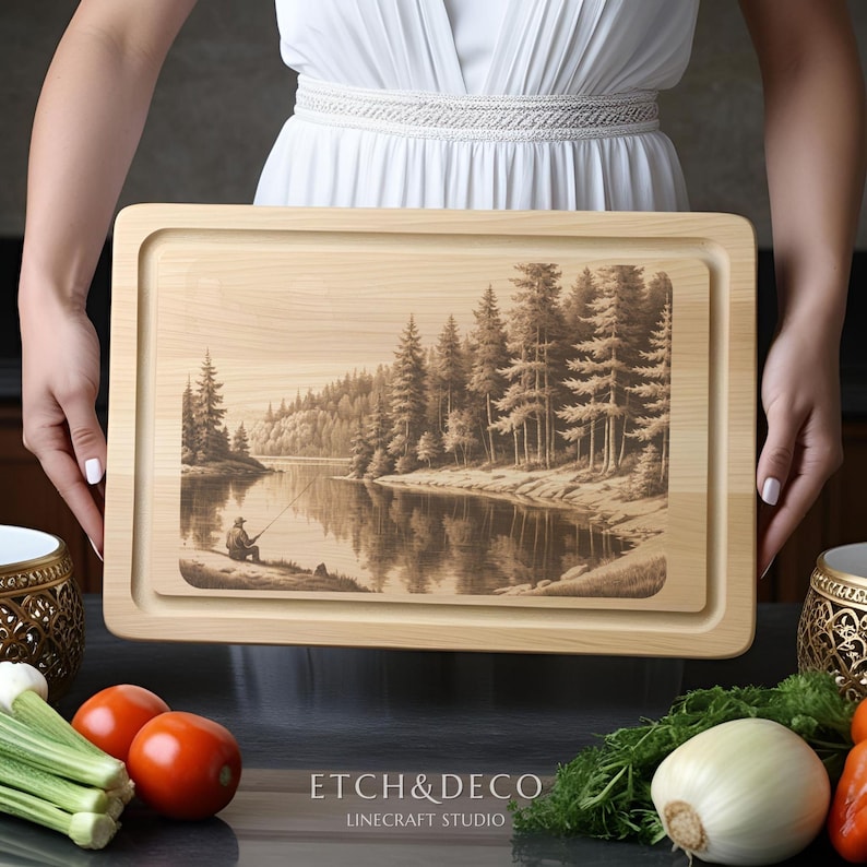 May include: A rectangular wooden cutting board with a recessed area. The board features an engraved landscape scene of a person fishing by a lake surrounded by trees. The text "ETCH&DECO" and "LINECRAFT STUDIO" are at the bottom.