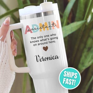 May include: White tumbler with a handle, featuring the word "Assistant" in colorful letters. Below, it reads "The only one who knows what's going on around here." A heart and the name "Veronica" are also displayed. A "SHIPS FAST!" sticker is visible.