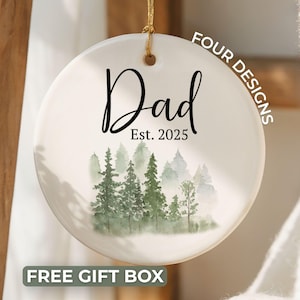 May include: A round, white ceramic ornament with the word "Dad" in black script and "Est. 2025" below it. A watercolor forest scene is at the bottom. The text "FOUR DESIGNS" and "FREE GIFT BOX" are also visible.