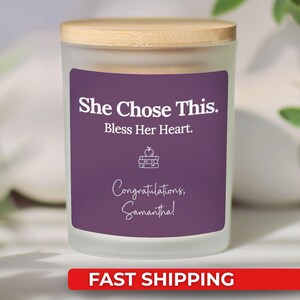 May include: A frosted glass candle with a wooden lid. The candle has a purple label with white text that reads "She Chose This. Bless Her Heart. Congratulations, Samantha!" A red banner at the bottom says "FAST SHIPPING".